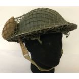 A WWII style British Brodie helmet with cam net and field dressing.