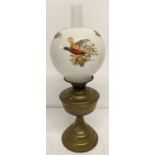 A vintage brass oil lamp with round glass opaque shade decorated with pheasants in flight.