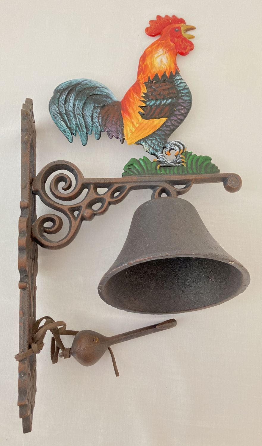 A painted cast metal wall hanging garden bell with cockerel detail.