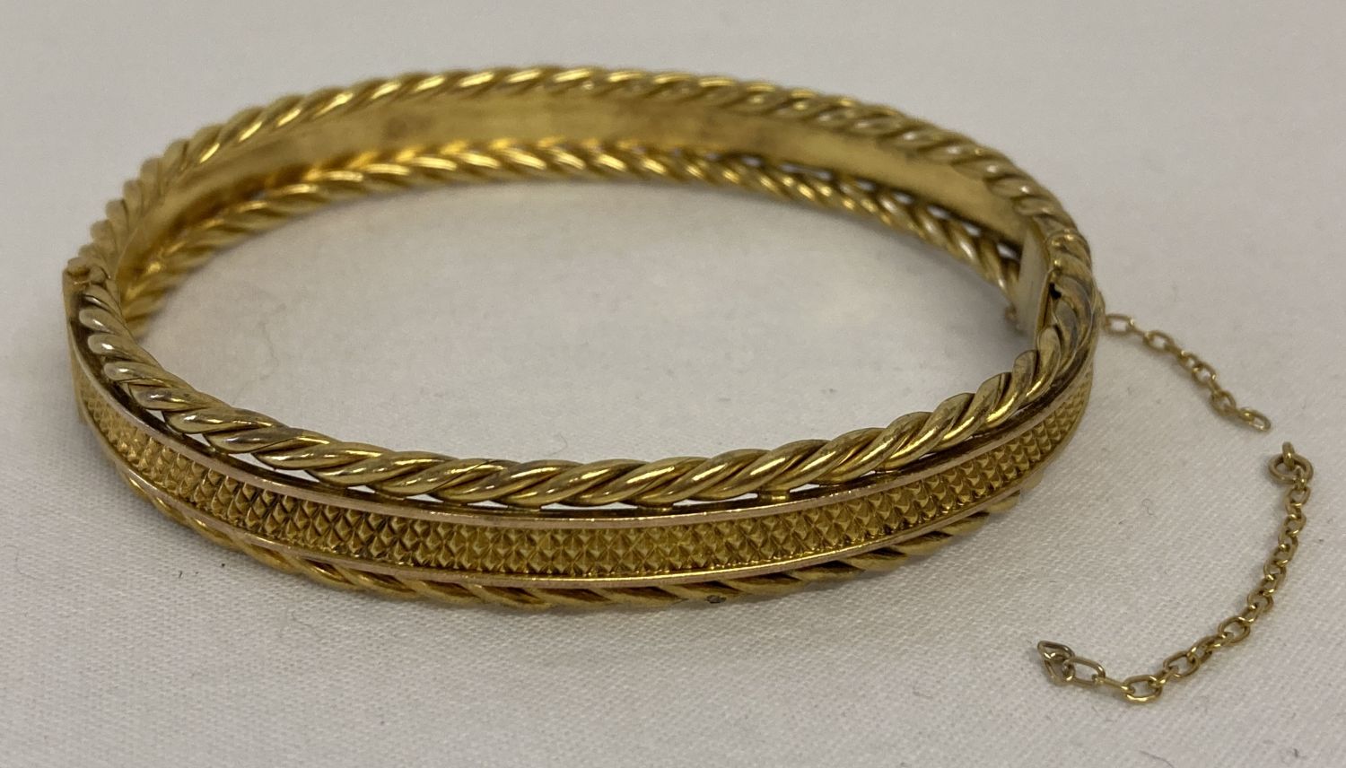 A gold bangle with diamond shaped decoration to centre and twisted rope details to both edges.