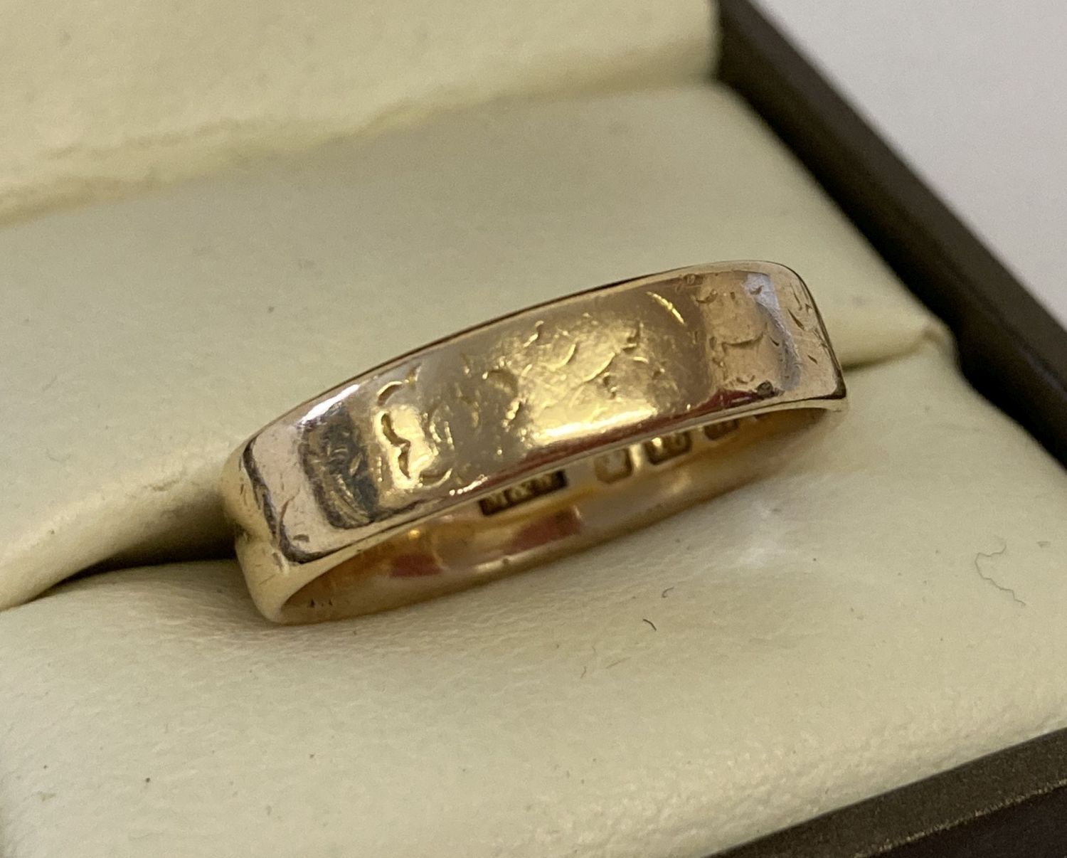 A 18ct gold wedding band with worn floral decoration.