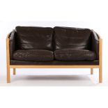 Stouby two seat settee, with curved arms and black leather cushions, raised on turned legsSome