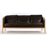 Stouby three seat settee, with curved arms and black leather cushions, raised on turned legsSome