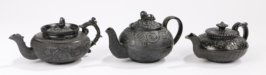 Three 19th Century black basalt bachelors teapots, the first surmounted by a reclining dog above a