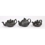 Three 19th Century black basalt bachelors teapots, the first surmounted by a reclining dog above a