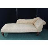 Victorian chaise longue, upholstered in a gold foliate decorated material, on turned reeded legs and