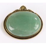 Jade brooch, the oval stone housed in a gilt setting with shell form pediment
