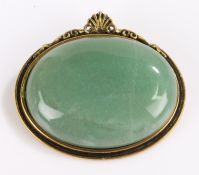 Jade brooch, the oval stone housed in a gilt setting with shell form pediment