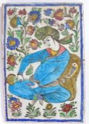 Persian Qajar pottery tile, of a seated figure pour from a bottle with a flower surround, 23cm x