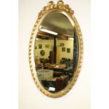 Oval bevelled wall mirror, with pierced tied ribbon foliate pediment, 37cm x 62cm