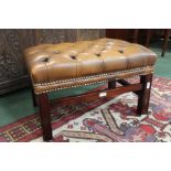 Brown leather footstool, the button seat raised on square legs and flattened stretchers