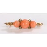 Unmarked yellow metal brooch set with three coral beads interspersed with pearls, 2.9g