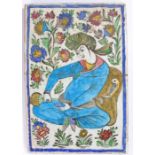 Persian Qajar pottery tile, of a seated figure pouring from a bottle, with a flower surround, 23cm x