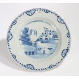 18th Century Delft charger, in blue and white with buildings near a river, an arched foliate edge to