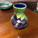 A Moorcroft vase designed with a purple flower and green background. Measures 10.5cm in height