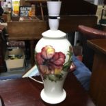 A William Moorcroft table lamp in the Hibiscus pattern against a white background. Has original