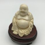An Oriental Meiji period laughing Buddha ivory carved deity. Sset on a hardwood stand with brass
