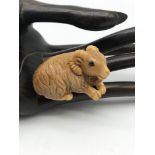 A Japanese hand carved Tagua nut netsuke figure of a goat laying down. Detailed with black bead