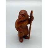 A Japanese hand carved netsuke of a Monkey God figure, Designed holding a staff and wearing a