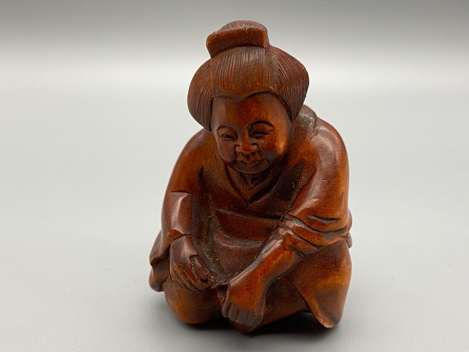 A Japanese hand carved netsuke of an elderly Geisha washing her feet. Signed by the artist.