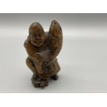 A Hand carved Japanese netsuke figure of a Older Gentleman holding a Koi Carp whilst standing on the