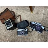 Three vintage cameras which include Kodak Brownie model c, Olympus Trip 35 & Praktica MTL3.