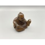 A Hand carved Japanese netsuke of an elderly gentleman sitting holding a mask. Signed by the artist.