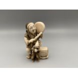 A Meiji Period ivory carved Japanese netsuke of a man beating a drum and his monkey dancing.