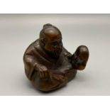 A Japanese hand carved netsuke of an elderly gentleman sat holding a mask. Signed to the base by the