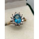 A Ladies 9ct gold ring set with an aquamarine stone off set by a clear stone cluster. [2.65grams]