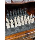 A Heavy hand carved slate chess board together with a set of oriental chess pieces made from resin.