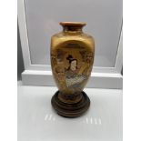 A Japanese Satsuma hand painted vase with hard wood stand. Designed with figures, dragon and gilt