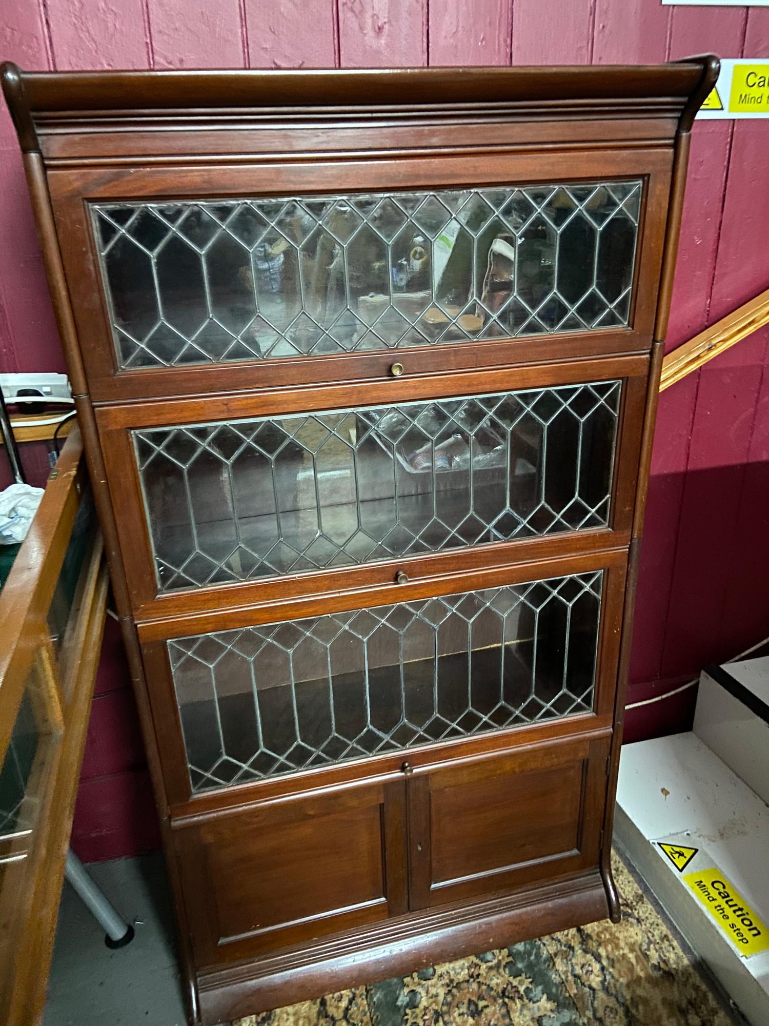 A Four section barristers bookcase designed with lead and glass lift up section doors. [155x87x35cm]