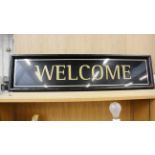 A black plastic framed 'Welcome' sign Dimensions 120cm(L) x 30cm(H)