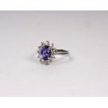 An 18k white gold tanzanite and diamond dress ring. Central oval free cut Tanzanite 8mm x 6mm with a