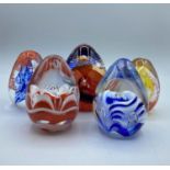 5 egg shaped glass paperweights with various patterns.