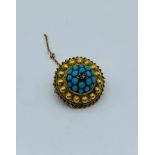 A yellow metal brooch with turquoise stones and it weighs 5.7g.