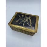 An Art Deco style brass cigarette box, harlequins smoking brass inlay on black wood top. size 12.5cm