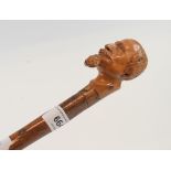 A folk art walking cane, the carved wood handle in the form of the head of a Victorian gentleman,