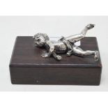 A silver coloured metal figure, of a fallen skater, on a hardwood base, 9.5 cm wide