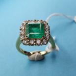 An 18ct yellow gold step cut emerald and diamond cluster ring. Emerald approx. 2.84ct, diamonds