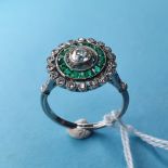 An Edwardian style platinum, emerald and diamond cluster ring. A central old-cut diamond (0.3ct,