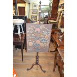 A George III mahogany pole screen, with an associated floral needlework panel, on a tripod base with