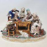A large continental porcelain group, figures around a table, a finger detached but present, 32 cm