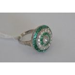 A platinum emerald and diamond ring, set with a central old cut diamond, surrounded by a halo of
