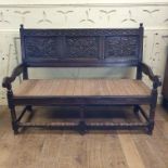 An oak settle, the three panel back carved flowers and foliage, on baluster turned front supports