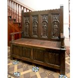 A Gothic oak box settle, the castellated top above four panels carved figures, the base with four