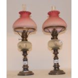 A pair of silver plated oil lamps, with opaque glass wells and pink glass shades, 50 cm high (2)