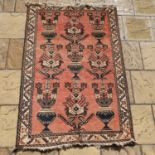 A red ground tribal carpet, main cream border, centre decorated with vases and stylised foliate