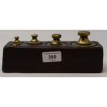 A set of five brass graduated weights, set in a wooden block, 20 cm wide